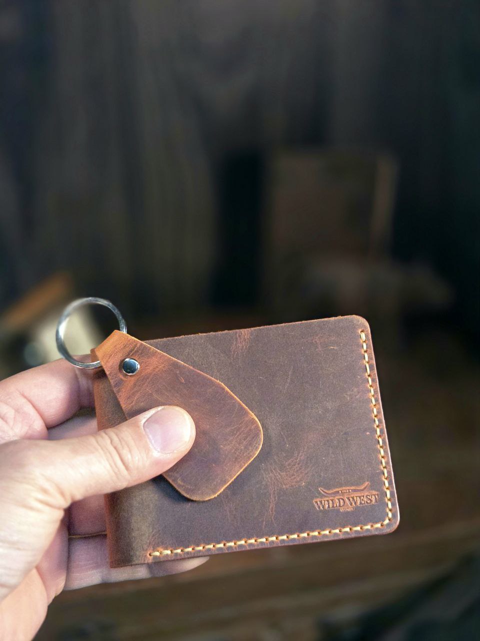El yapımı kahverengi deri kartlık, anahtarlıkla birlikte elde tutulurken görülüyor. Üzerinde Wild West Crafted logosu yer alıyor